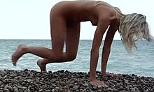 Blonda care pozează complet goală pe o plajă stâncoasă